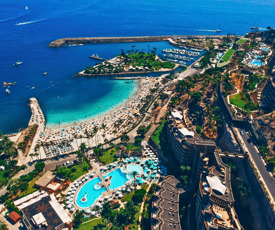 Amadores Beach crescent bay with calm turquoise water protected by breakwaters, white sand lined with sunbeds and a seafront promenade, Mogán, southwest Gran Canaria.
