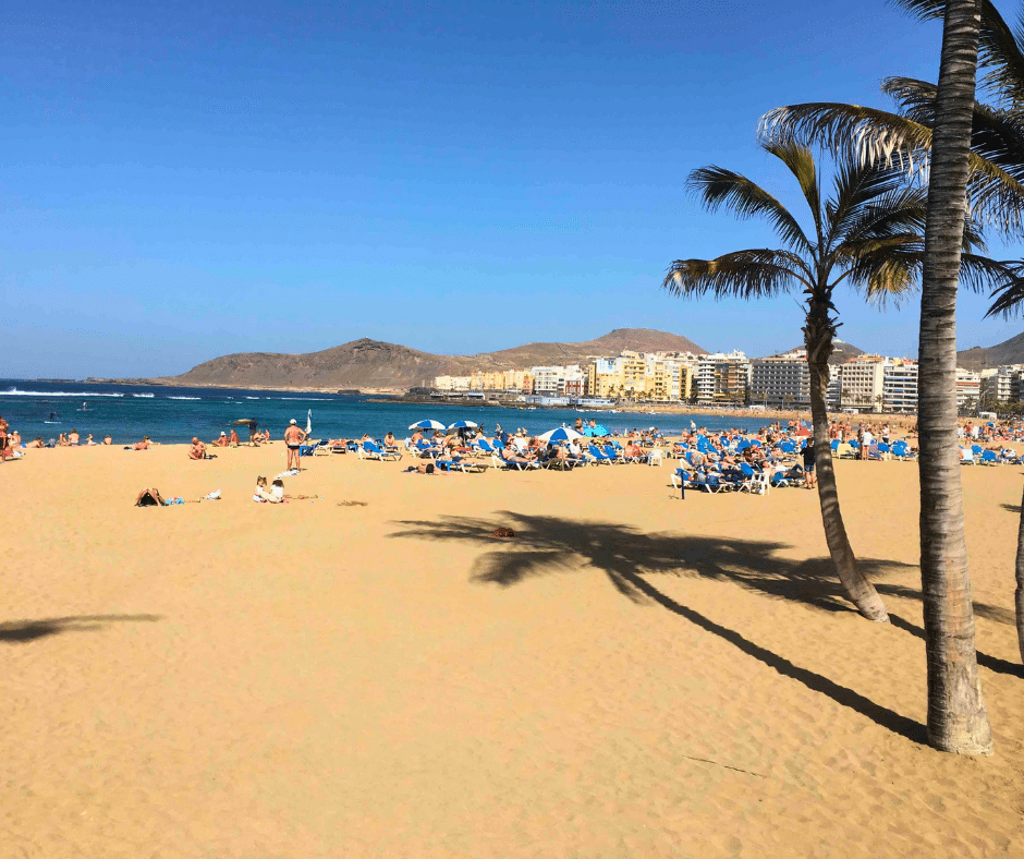 Las Canteras at low tide with La Barra reef calming a clear lagoon; snorkellers by Playa Chica and the seafront promenade of Las Palmas de Gran Canaria.