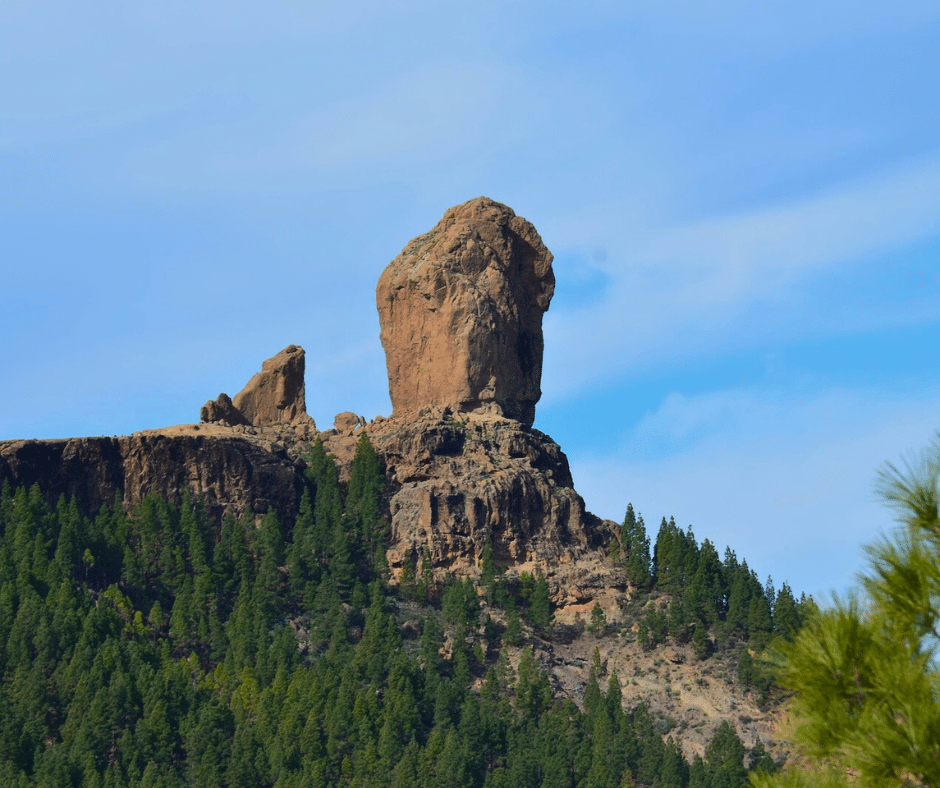 Roque Nublo volcanic monolith at golden hour, pine-clad highlands and a sea of clouds below, central Gran Canaria.